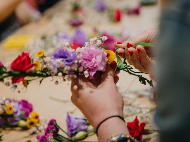 A person is stood at a table filled with fresh flowers, making a flower crown